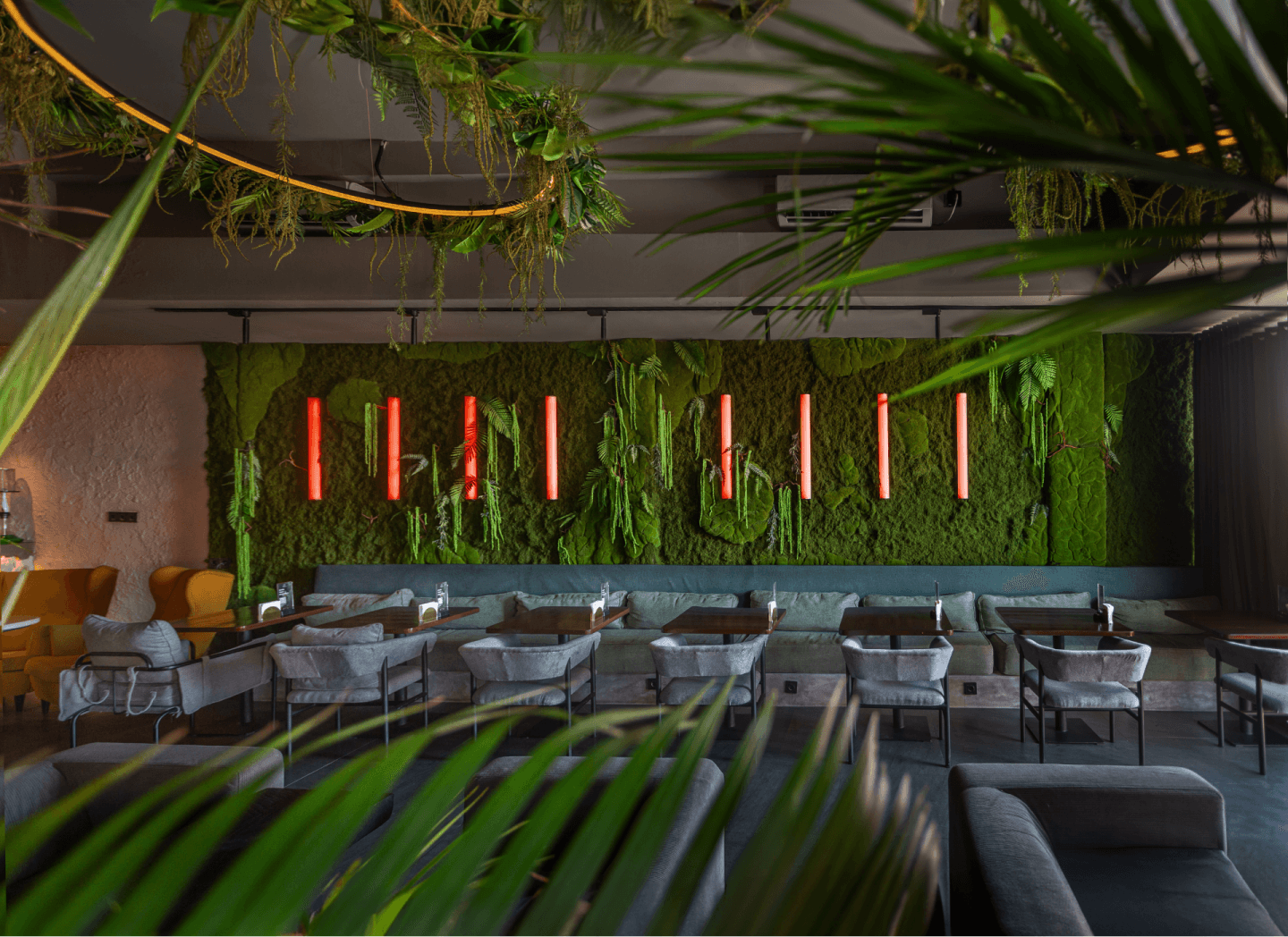 Lounge seating among palms, with red neon strips on a green wall